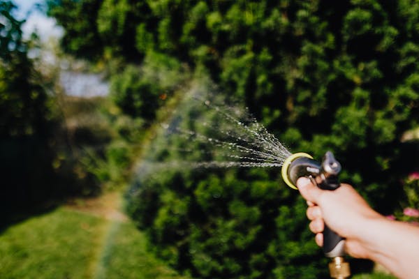 A hand holds a water sprayer and creates a rainbow in the sky